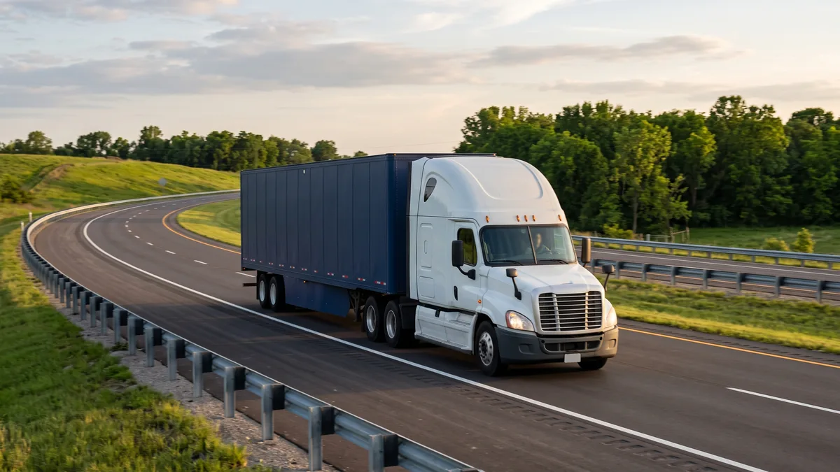 A plain semi truck with an unmarked navy box trailer traveling a curving interstate past green embankments near O'Fallon, Missouri